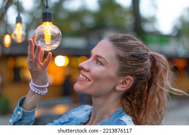 Young Caucasian Woman Holding Energy Efficient LED String Light Bulb At Outdoors