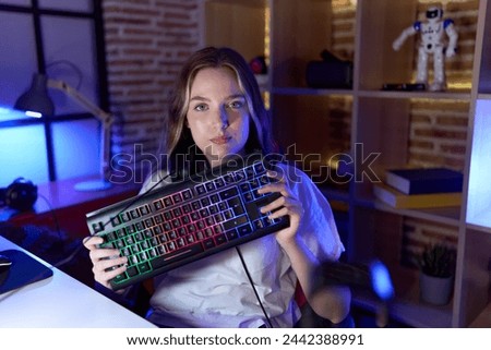 Young caucasian woman holding gamer keyboard relaxed with serious expression on face. simple and natural looking at the camera. 