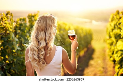 Young caucasian woman holding a glass of red wine in vineyard on sunny day, back view - Vinification, vine-growing and wine-tasting concept with a millennial young adult girl - Powered by Shutterstock