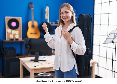 Young Caucasian Woman Holding Guitar Case Pointing Thumb Up To The Side Smiling Happy With Open Mouth 