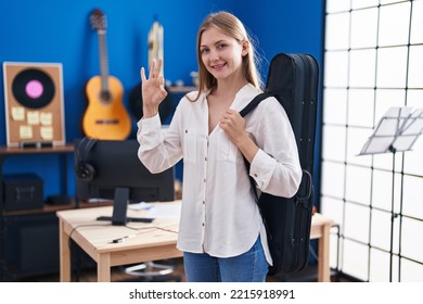 Young Caucasian Woman Holding Guitar Case Doing Ok Sign With Fingers, Smiling Friendly Gesturing Excellent Symbol 