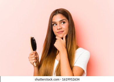 Young Caucasian Woman Holding An Hairbrush Looking Sideways With Doubtful And Skeptical Expression.