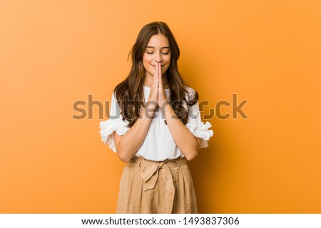 Young caucasian woman holding hands in pray near mouth, feels confident.