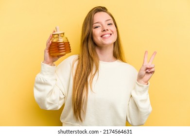 Young Caucasian Woman Holding A Honey Isolated On Yellow Background Joyful And Carefree Showing A Peace Symbol With Fingers.