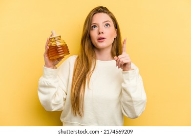 Young Caucasian Woman Holding A Honey Isolated On Yellow Background Pointing Upside With Opened Mouth.