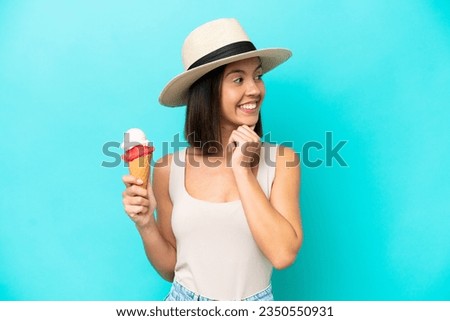 Young caucasian woman holding an ice cream isolated on blue background looking up while smiling