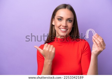 Young caucasian woman holding invisible braces pointing to the side to present a product