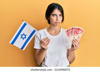 Young Caucasian Woman Holding Israel Flag And Shekels Banknotes Depressed And Worry For Distress, Crying Angry And Afraid. Sad Expression. 