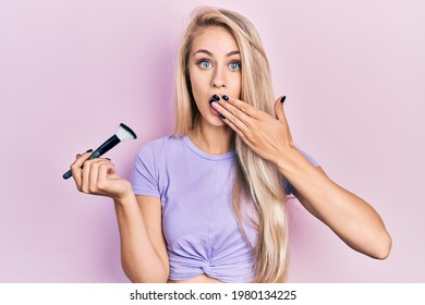 Young Caucasian Woman Holding Makeup Brush Covering Mouth With Hand, Shocked And Afraid For Mistake. Surprised Expression 