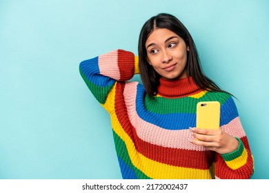 Young Caucasian Woman Holding Mobile Phone Isolated On Blue Background Touching Back Of Head, Thinking And Making A Choice.