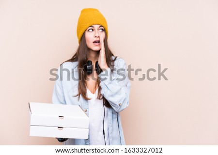 Young caucasian woman holding pizzas isolated is saying a secret hot braking news and looking aside