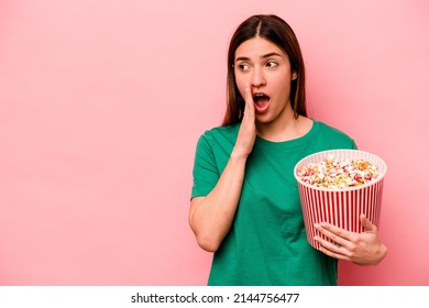 Young Caucasian Woman Holding Popcorn Isolated On Pink Background Is Saying A Secret Hot Braking News And Looking Aside