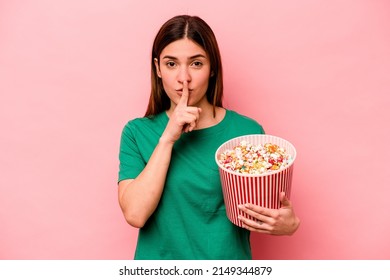 Young Caucasian Woman Holding Popcorn Isolated On Pink Background Keeping A Secret Or Asking For Silence.