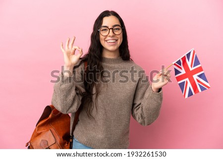 Young caucasian woman holding an United Kingdom flag isolated on pink background showing ok sign with fingers