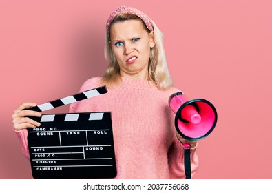 Young Caucasian Woman Holding Video Film Clapboard And Megaphone Clueless And Confused Expression. Doubt Concept. 