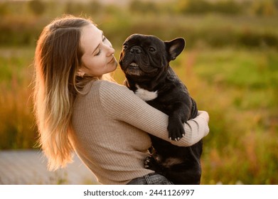 Young Caucasian woman holds and hugs dog in park during walk at sunset. Beloved dog is in arms of owner. Concept of pet care, love for pet, affection - Powered by Shutterstock