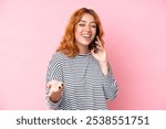 Young caucasian woman isolated on pink background keeping a conversation with the mobile phone with someone