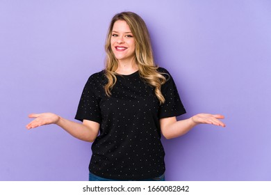 Young caucasian woman isolated on purple background makes scale with arms, feels happy and confident. - Shutterstock ID 1660082842