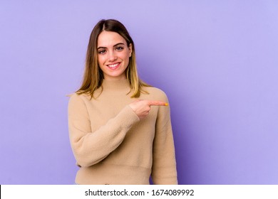 Young caucasian woman isolated on purple background smiling and pointing aside, showing something at blank space.