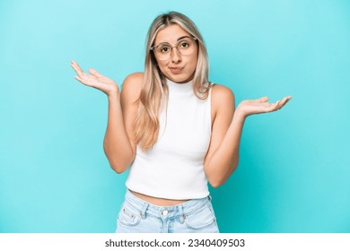 Young caucasian woman isolated on blue background having doubts while raising hands - Shutterstock ID 2340409503