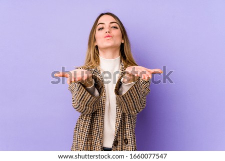 Young caucasian woman isolated on purple background folding lips and holding palms to send air kiss.