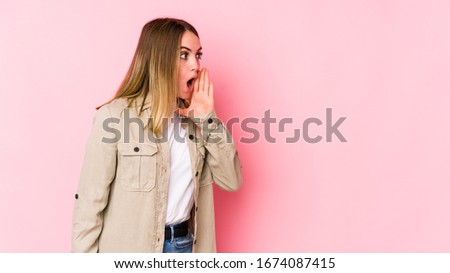 Young caucasian woman isolated on pink background is saying a secret hot braking news and looking aside
