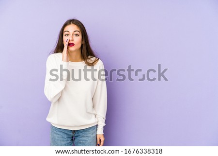 Young caucasian woman isolated on purple background is saying a secret hot braking news and looking aside