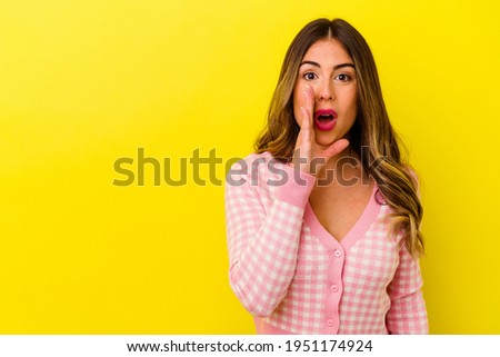 Young caucasian woman isolated on yellow background is saying a secret hot braking news and looking aside
