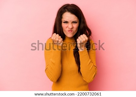 Young caucasian woman isolated on pink background showing fist to camera, aggressive facial expression.