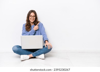 Young caucasian woman with a laptop sitting on the floor isolated on white background pointing to the side to present a product - Powered by Shutterstock