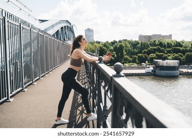 young Caucasian woman leans on bridge railing, taking break of workout in city.Female dressed in fitness attire,listening to online music through earphones on smartphone.sunny weather, relaxing moment - Powered by Shutterstock