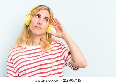 Young Caucasian Woman Listening To Music Isolated On Blue Background Touching Back Of Head, Thinking And Making A Choice.