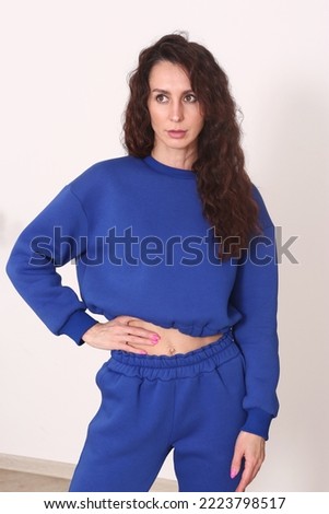 young caucasian woman with long curly brown hair in blue hoodie suit closeup photo on white wall background