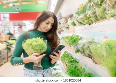 Young Caucasian Woman With Long Hair Buying Greens In The Supermarket Checking The List By Phone
