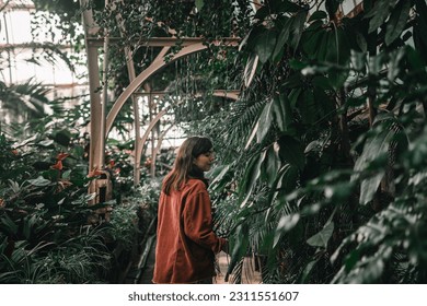 young caucasian woman with long hair and brown jacket among the greenery and plants of a large indoor botanic garden, botanic garden christchurch, new zealand - Shutterstock ID 2311551607