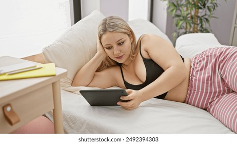 A young caucasian woman lounges in her bedroom, absorbed in her tablet while relaxing in casual wear. - Powered by Shutterstock