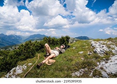 Young Caucasian Woman Lying Down And Taking A Rest In The Grass On A Mountain Peak With Blue Sky And Clouds Above