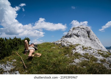 Young Caucasian Woman Lying Down And Taking A Rest In The Grass On A Mountain Peak With Blue Sky And Clouds Above