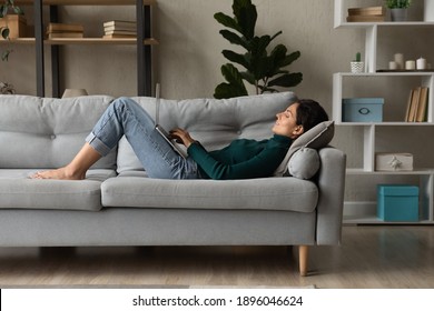 Young Caucasian Woman Lying On Couch In Living Room Work Online On Laptop Gadget. Millennial Female Relax Rest On Sofa At Home Look At Computer Screen Text Message On Device. Communication Concept.
