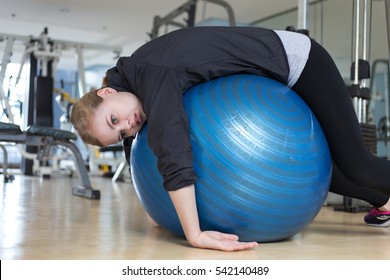 Young Caucasian Woman Lying On Blue Gymnastic Ball Looking Exhausted, Tired, Bored And Weary At The Gym