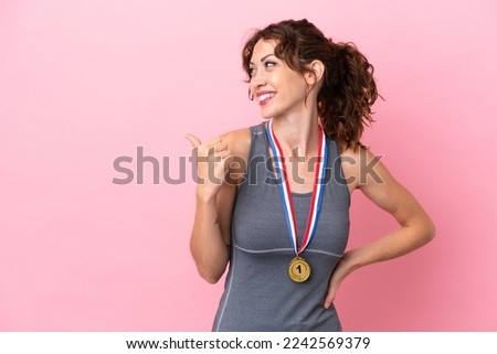 Young caucasian woman with medals isolated on pink background pointing to the side to present a product