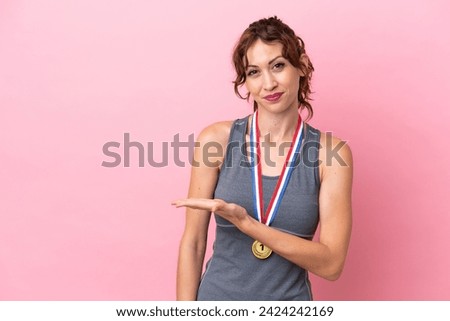 Young caucasian woman with medals isolated on pink background presenting an idea while looking smiling towards