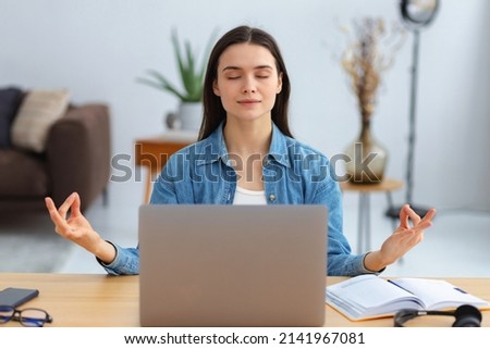 Young caucasian woman meditating eyes closed thinking of good things and focusing on positive feelings and emotions sitting in a modern office or at home