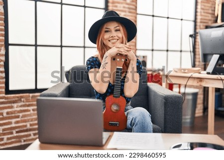 Young caucasian woman musician smiling confident holding ukulele at music studio