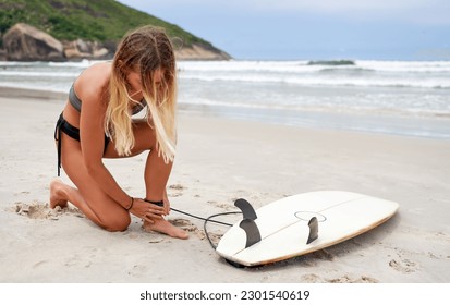 young caucasian woman on the beach putting on the leg surf leash or leg rope to go surfing the waves in Brazil	 - Powered by Shutterstock