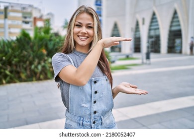 Young Caucasian Woman Outdoors Gesturing With Hands Showing Big And Large Size Sign, Measure Symbol. Smiling Looking At The Camera. Measuring Concept. 