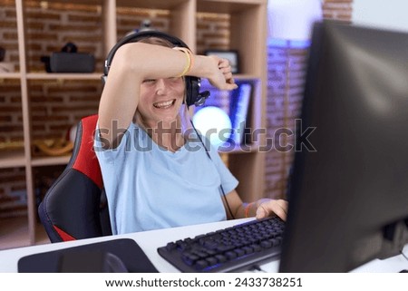 Young caucasian woman playing video games wearing headphones covering eyes with arm smiling cheerful and funny. blind concept. 