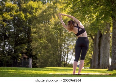 Young caucasian woman practising yoga in green parc peaceful environment in Switzerland standing side stretch pose