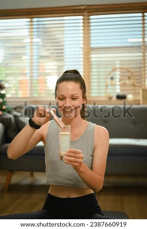 Young caucasian woman preparing healthy supplement after exercise dissolving collagen powder in glass of water.