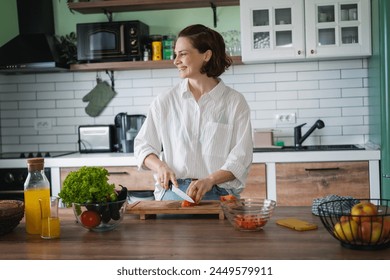 Young Caucasian woman preparing salad from green fresh vegetables while standing in the kitchen at home - Powered by Shutterstock